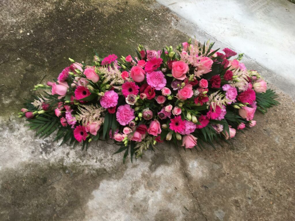 Dessus de cercueil tons rose soutenu avec des roses, des germinis, du lisianthus et de l’alstromeria